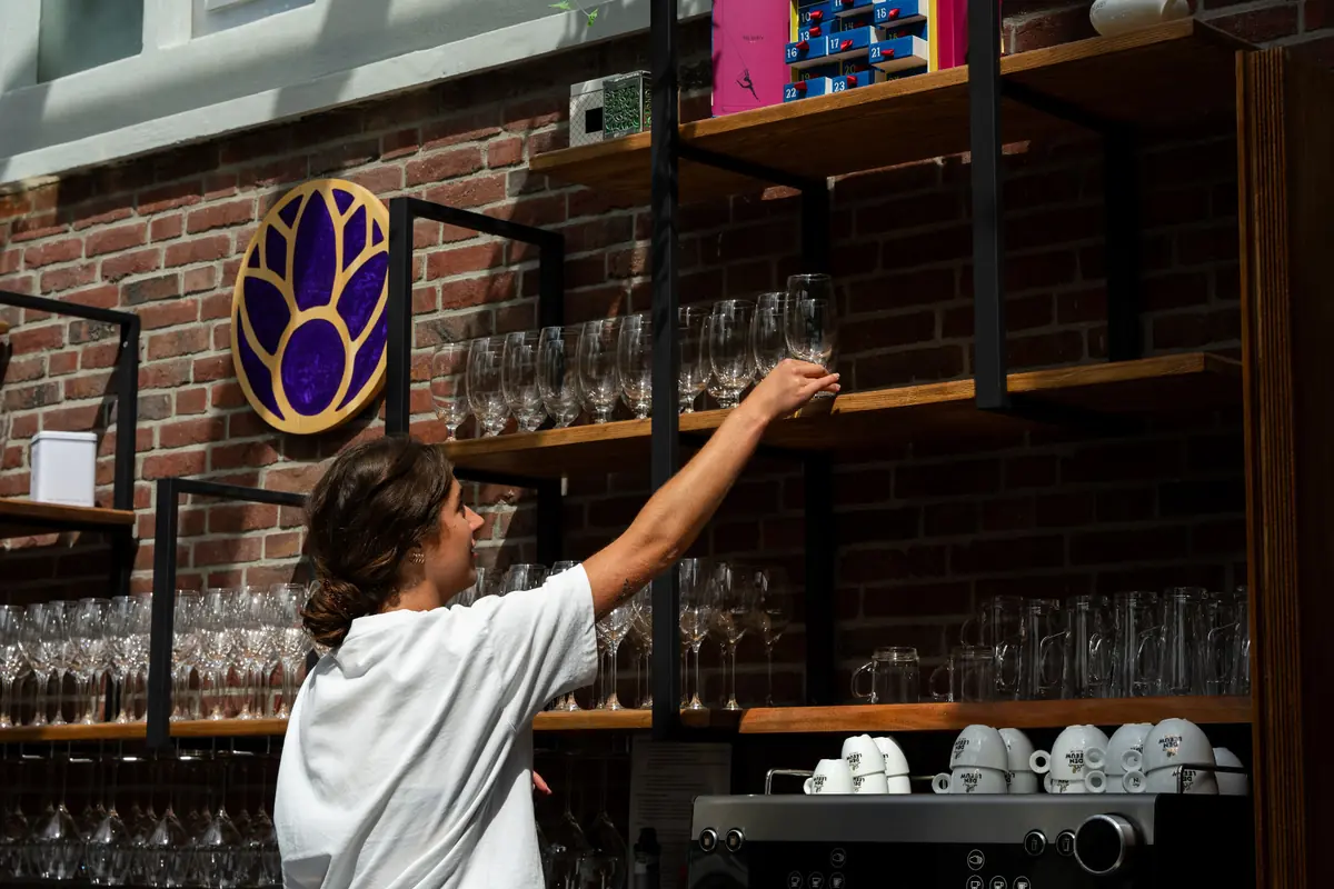 Medewerker van Brasserie Lenny pakt een wijnglas van het rek achter de bar in Amsterdam Oost.