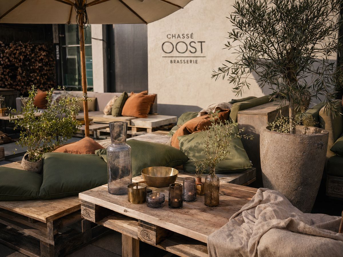 Loungehoek met olijfgroene kussens, brasseriedetails en olijfboom.